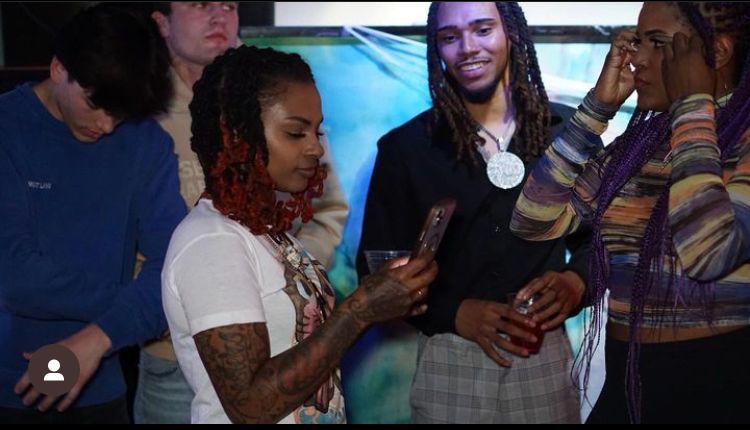 A group of people are standing around a woman holding a cell phone.