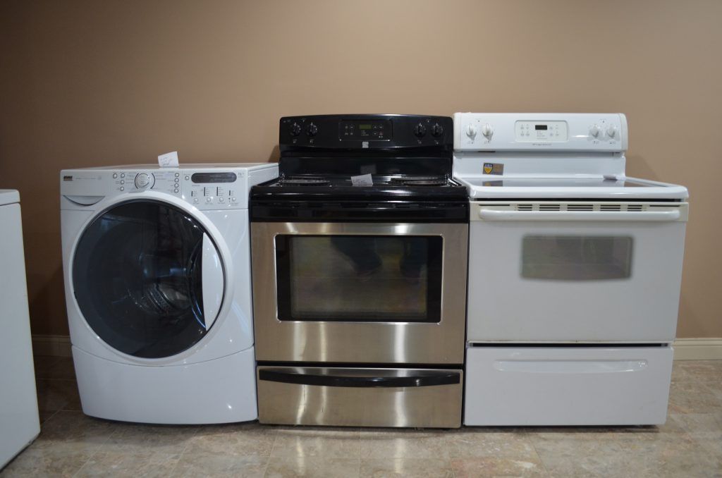 A washer, dryer, stove and oven are lined up in a room