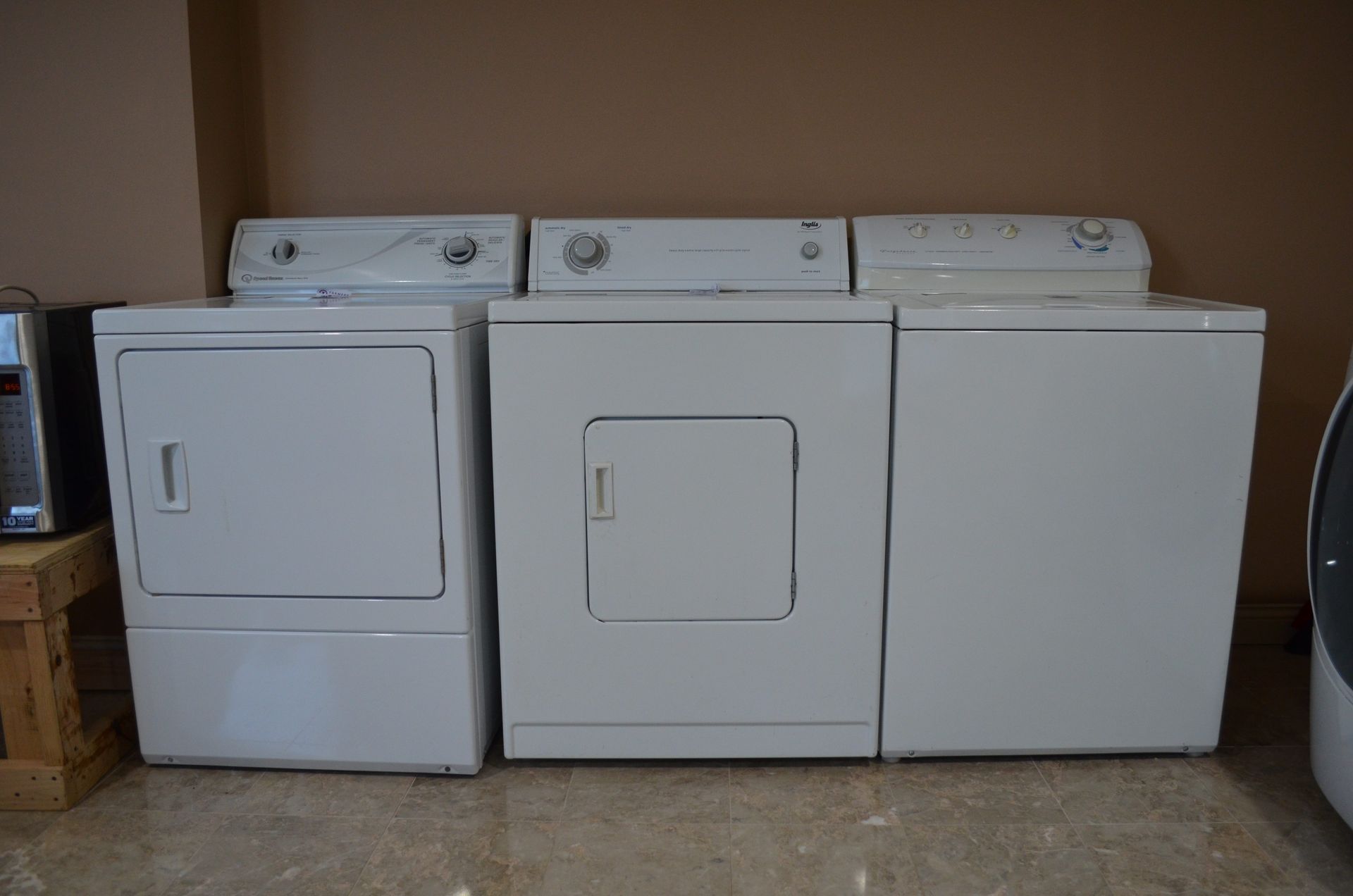 Three white washers and dryers are sitting next to each other in a laundry room.