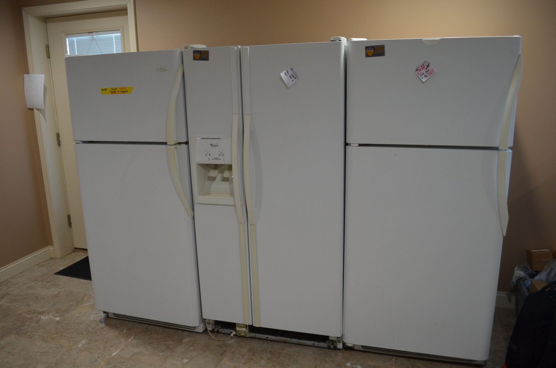 Three white refrigerators are sitting next to each other in a room.