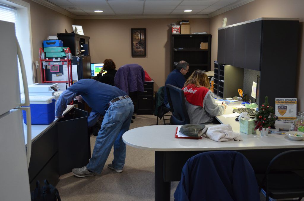 A group of people are working in a room with a refrigerator