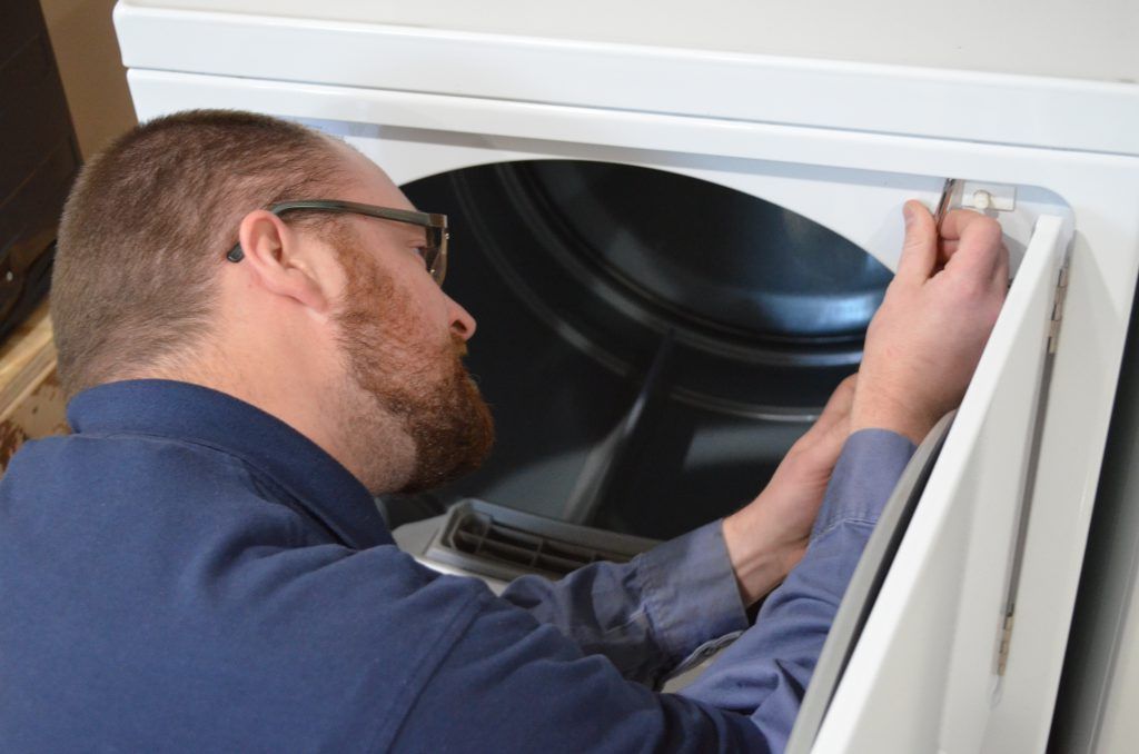 A man is working on a washer and dryer