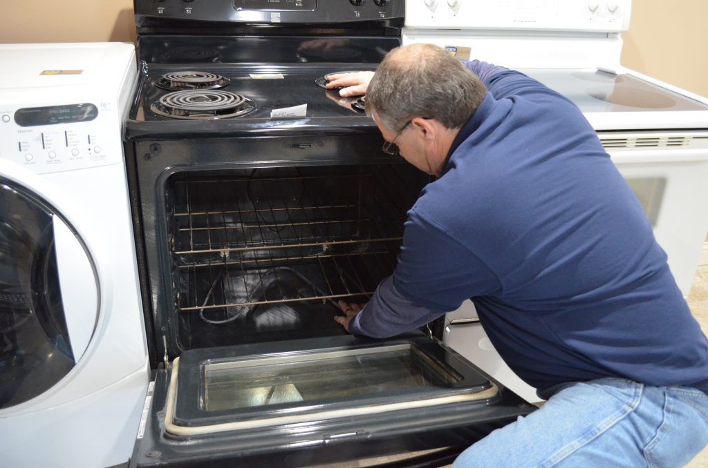 A man in a blue shirt is working on an oven