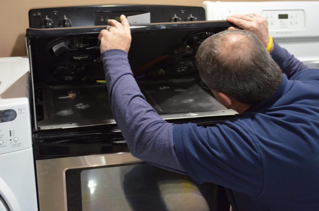 A man in a blue shirt is working on a stove
