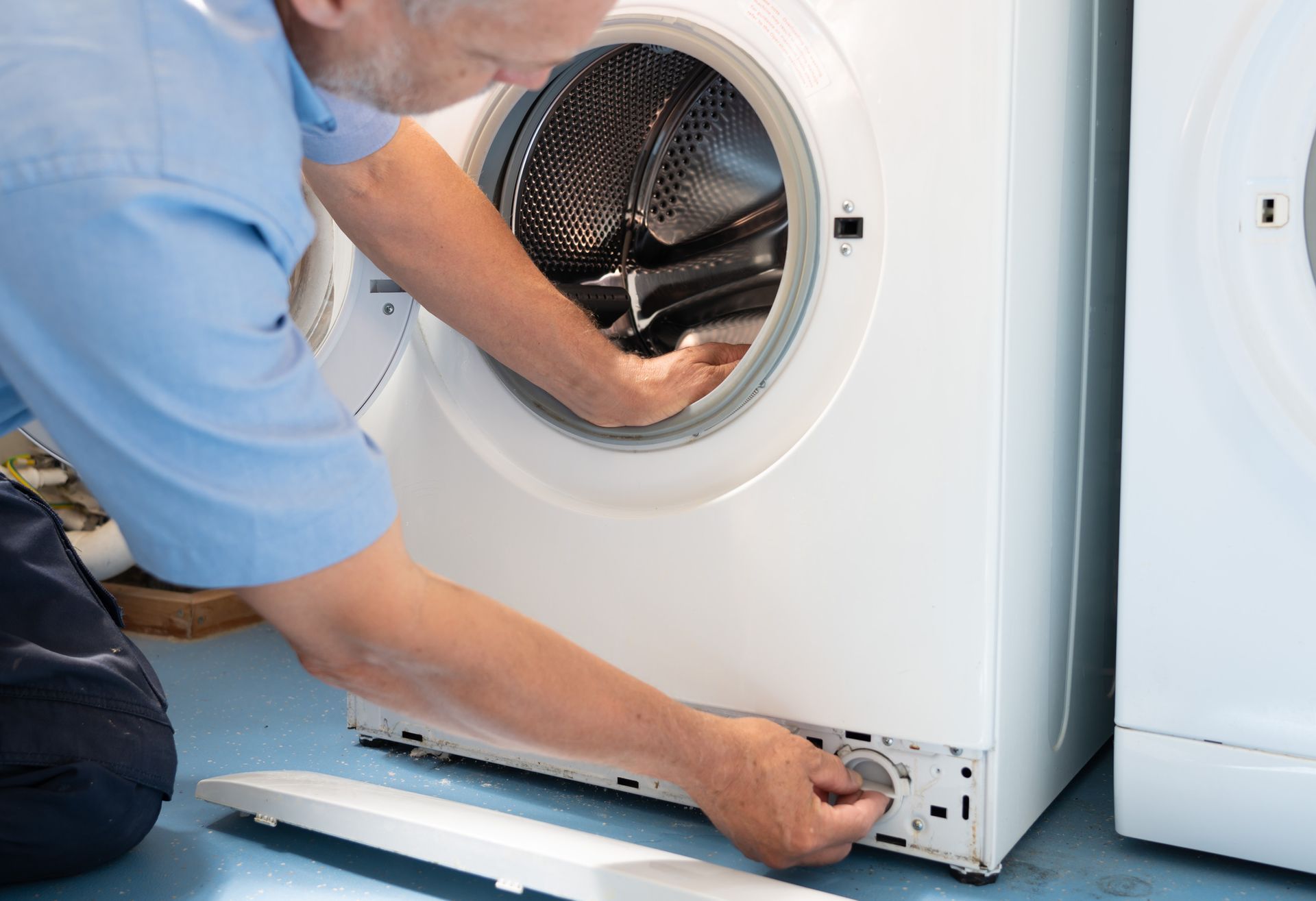 Person repairs a washing machine, working on the lower front panel with the door open.