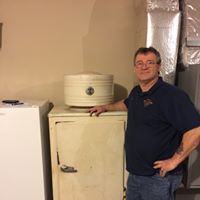 A man is standing next to an old refrigerator in a basement