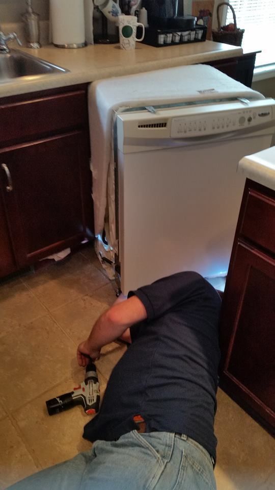 A man is laying on the floor fixing a dishwasher in a kitchen