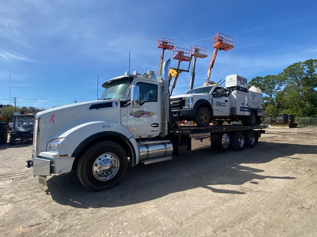 White truck hauling a smaller vehicle with three aerial lifts on a sunny day.
