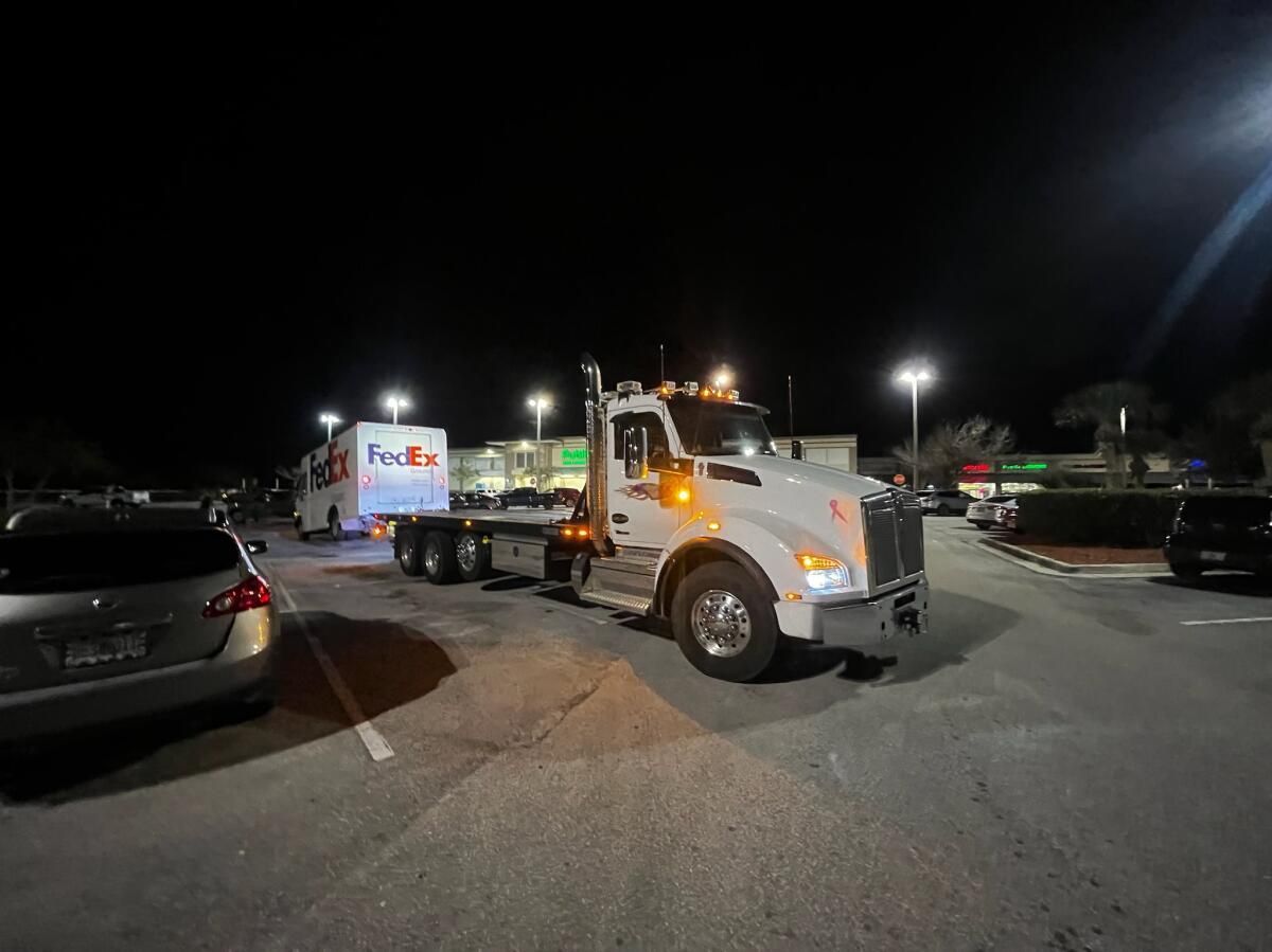 A FedEx trailer being pulled by a white semi-truck in a parking lot at night.