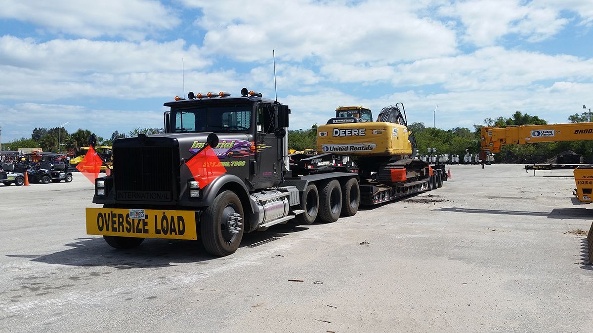 Black semi-truck hauling yellow excavator on a flatbed trailer, labeled 