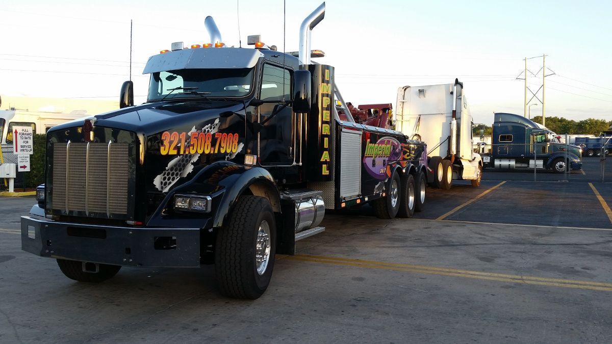 Black tow truck with bright decals, parked at a truck stop.