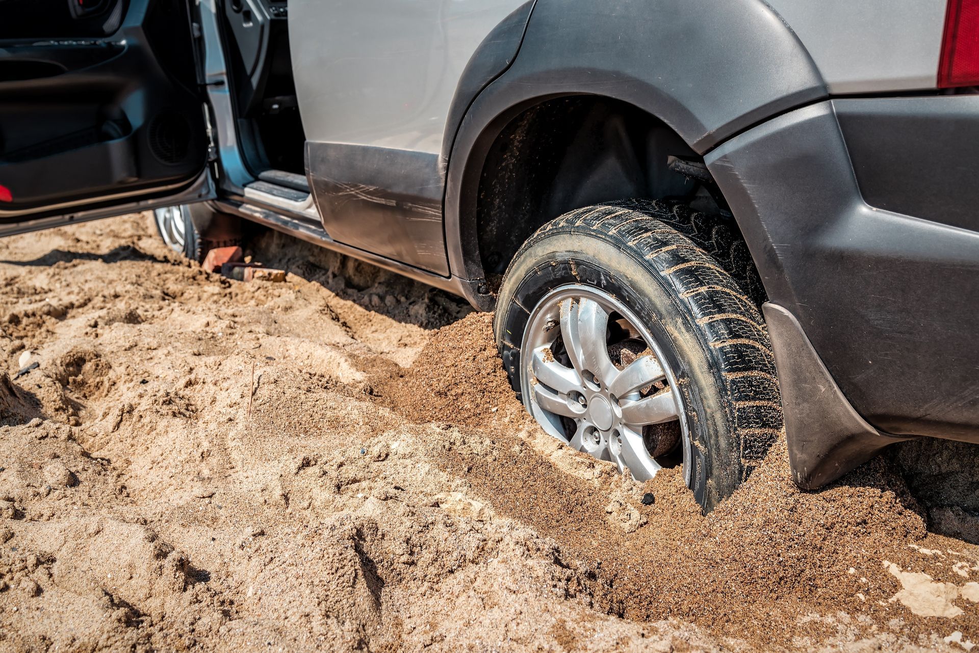 SUV stuck in deep mud with rear wheel buried in a sandy off-road ditch