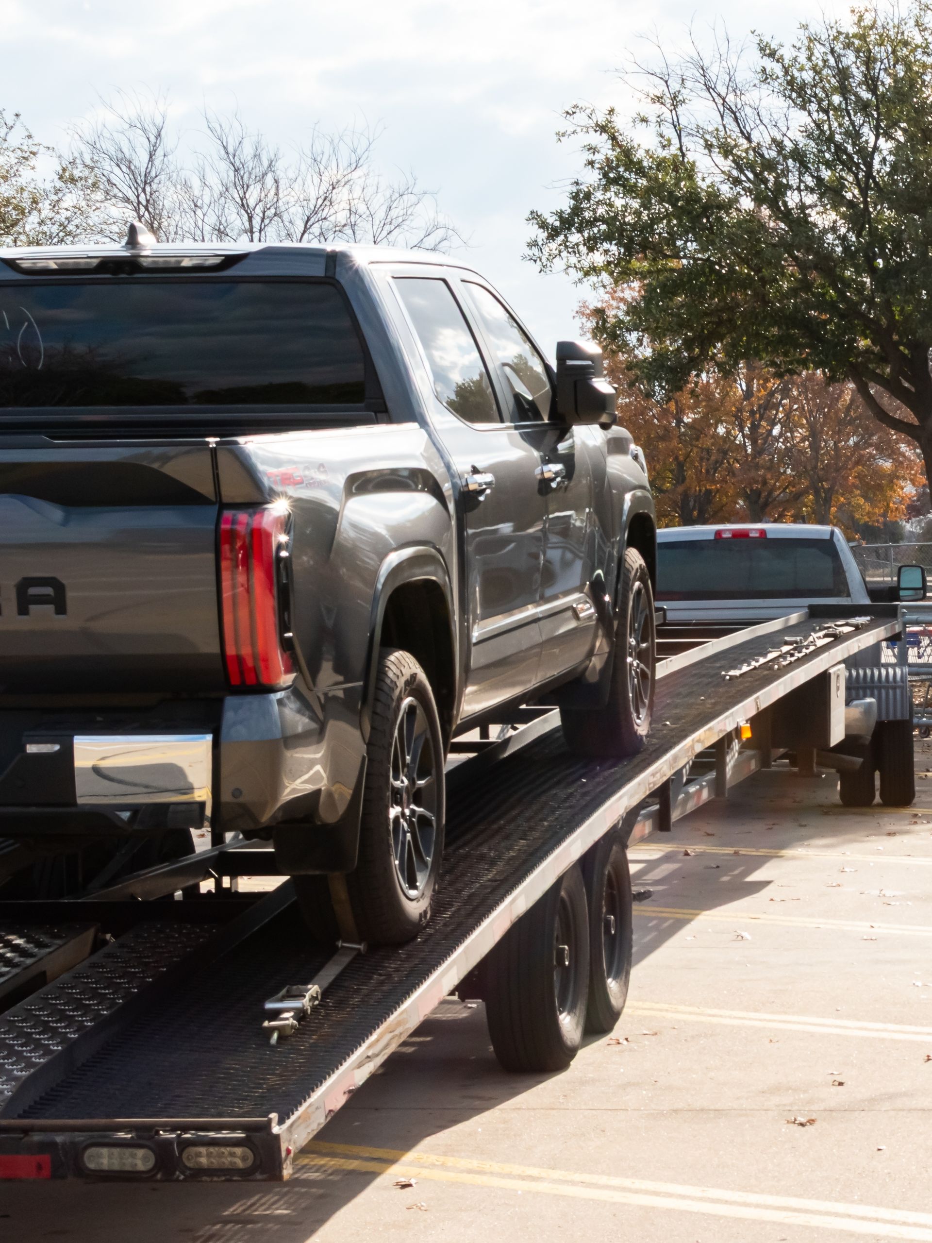 Black pickup truck loaded on a flatbed tow trailer on a street.