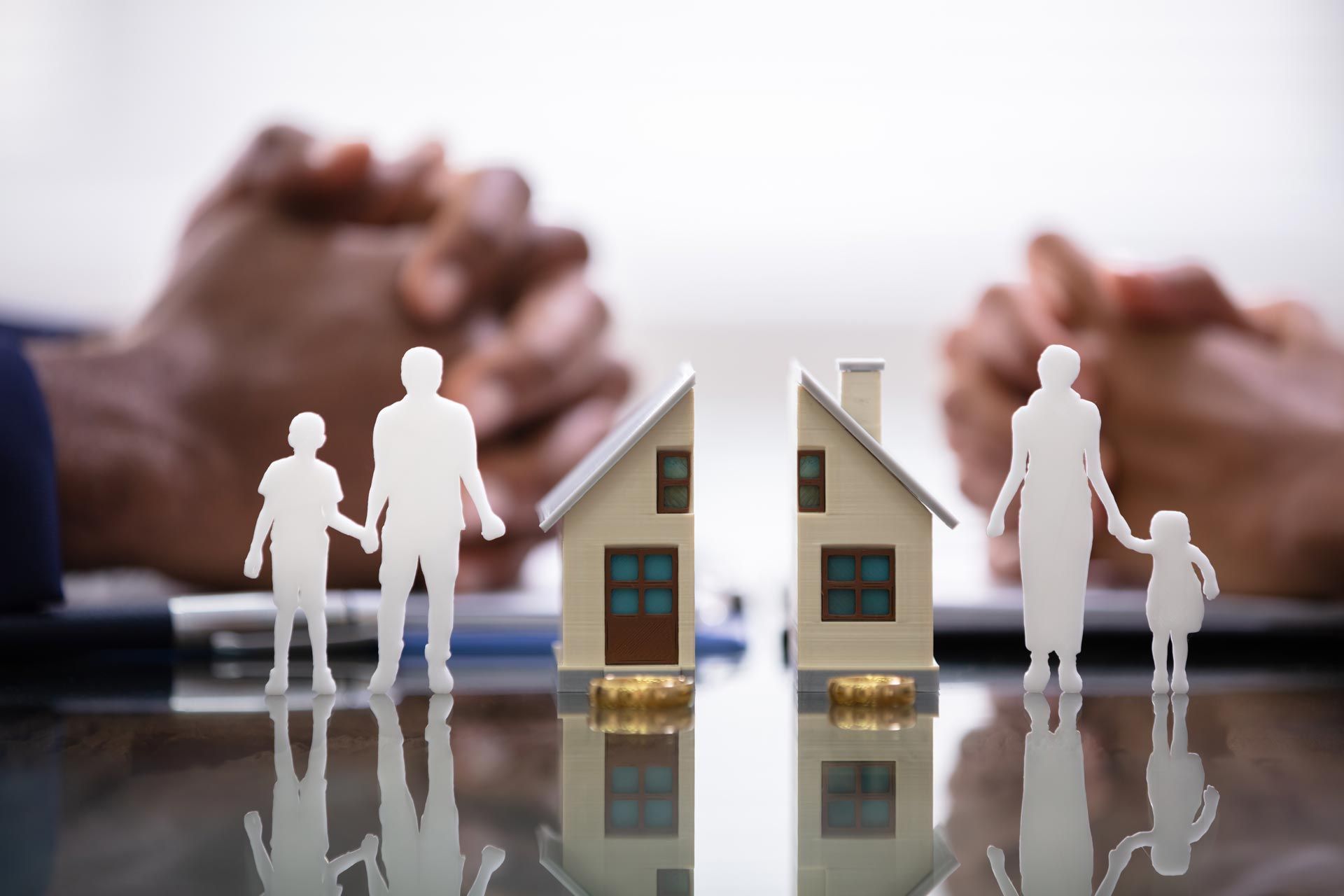 Paper family and split house halves between two clasped hands, symbolizing custody