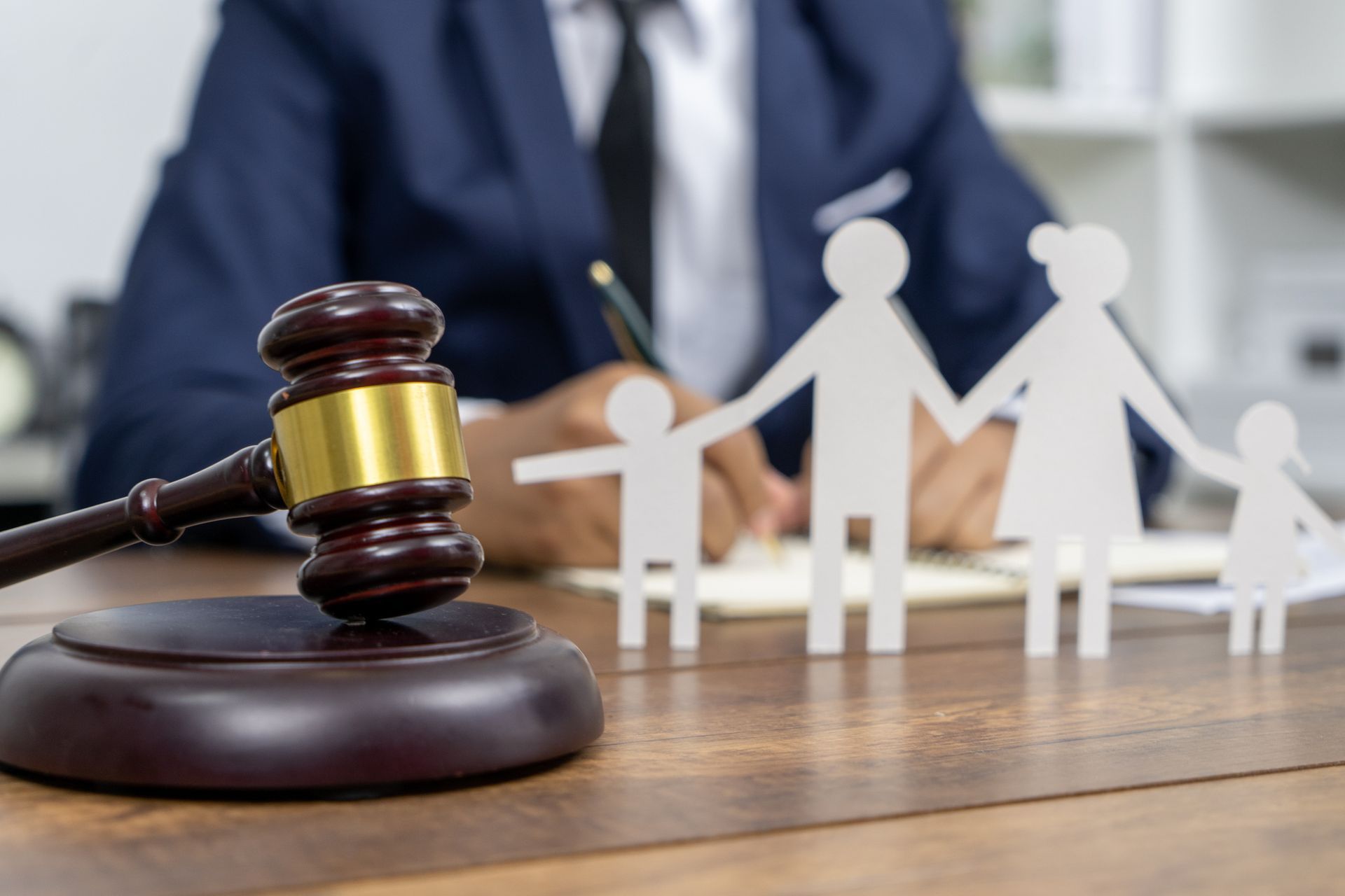 Family law attorney writing documents with gavel and paper family cutouts symbolizing legal support.