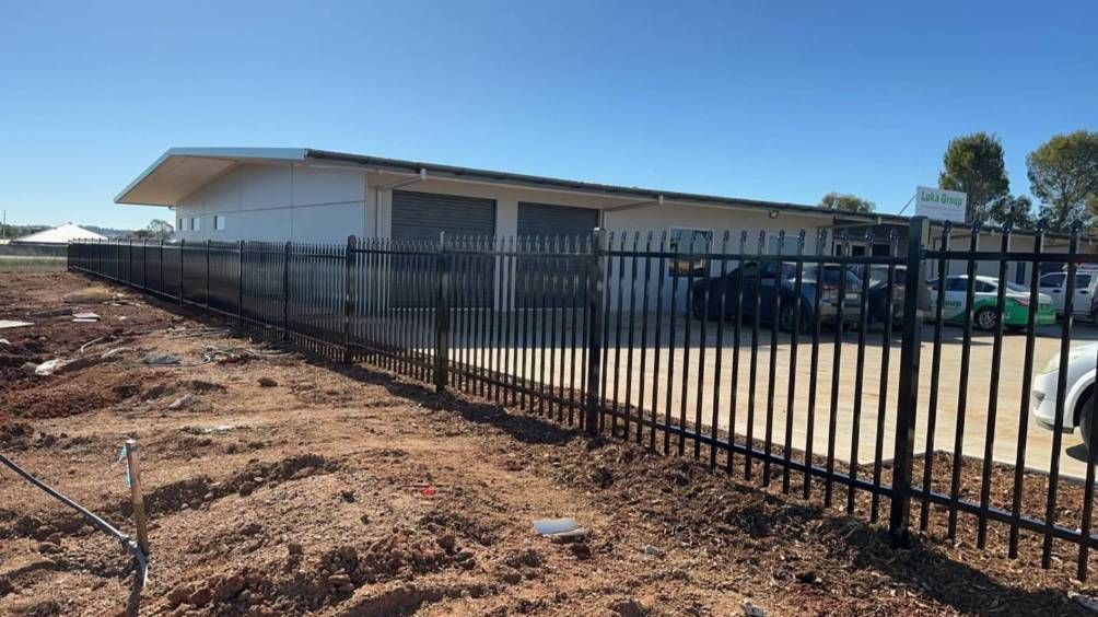 A Black Metal Fence Is Surrounding A Building With Cars Parked In Front Of It — Dubbo Allfence in Dubbo, NSW