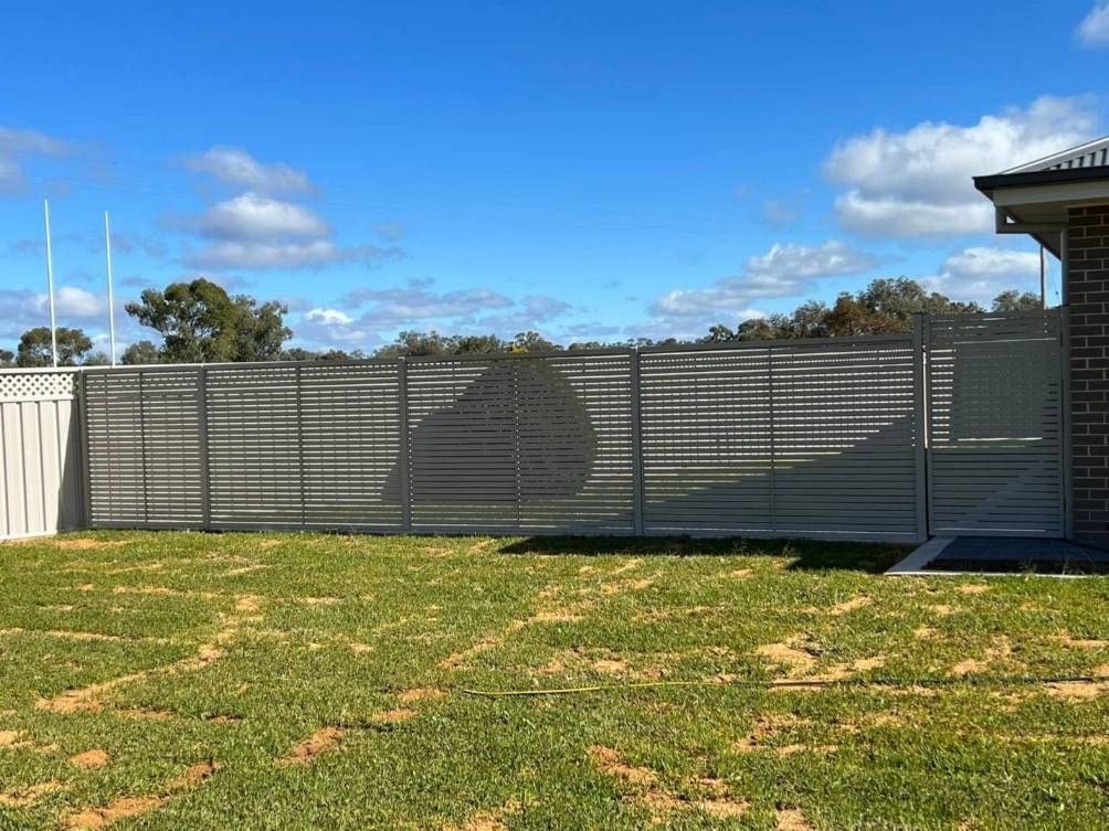 A Fence Is Surrounding A Lush Green Field In Front Of A House — Dubbo Allfence in Dubbo, NSW