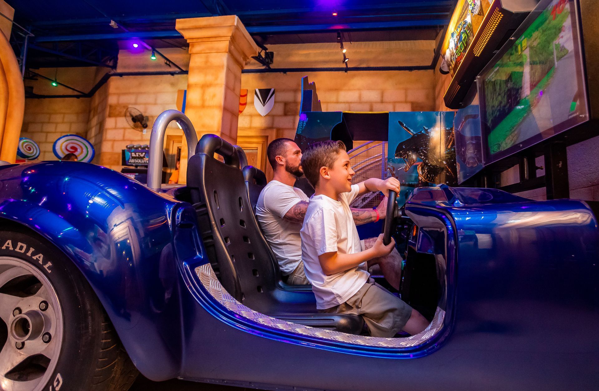 Um homem e um menino estão sentados em um carro azul jogando videogame.