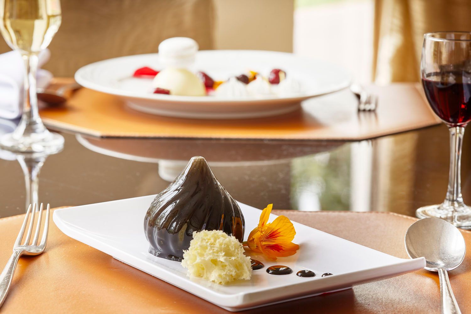 Prato de sobremesa com figo, flor e molho; mesa posta com taças de vinho e outro prato.