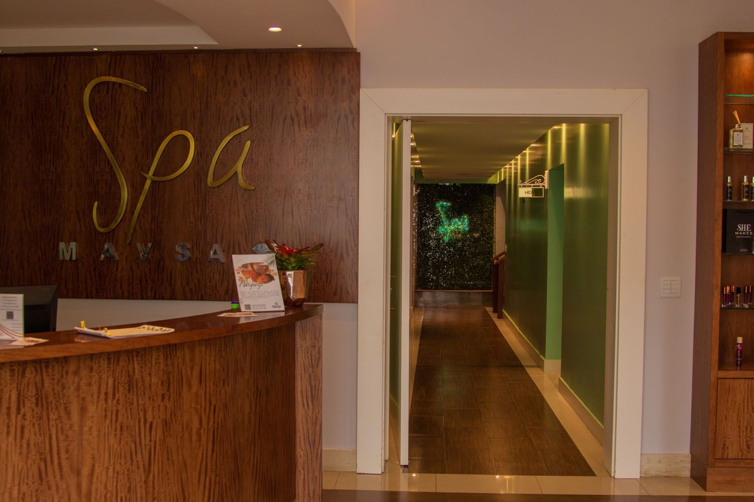 Área de recepção do spa com balcão de madeira escura, porta para um corredor com paredes verdes e letras douradas