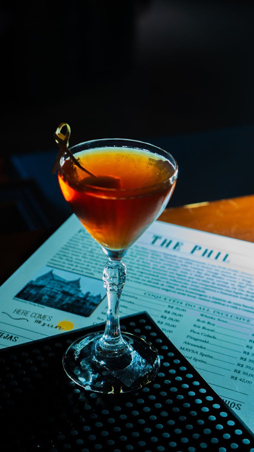 Coquetel em uma taça com haste e guarnição de cereja, no menu de um bar.