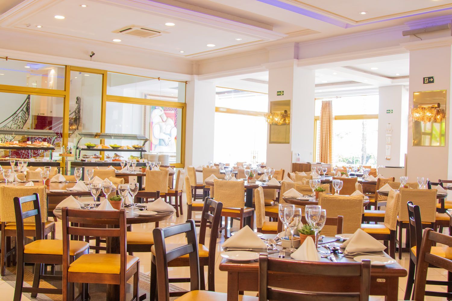 Interior do restaurante com mesas dispostas para jantar, bufê ao fundo.