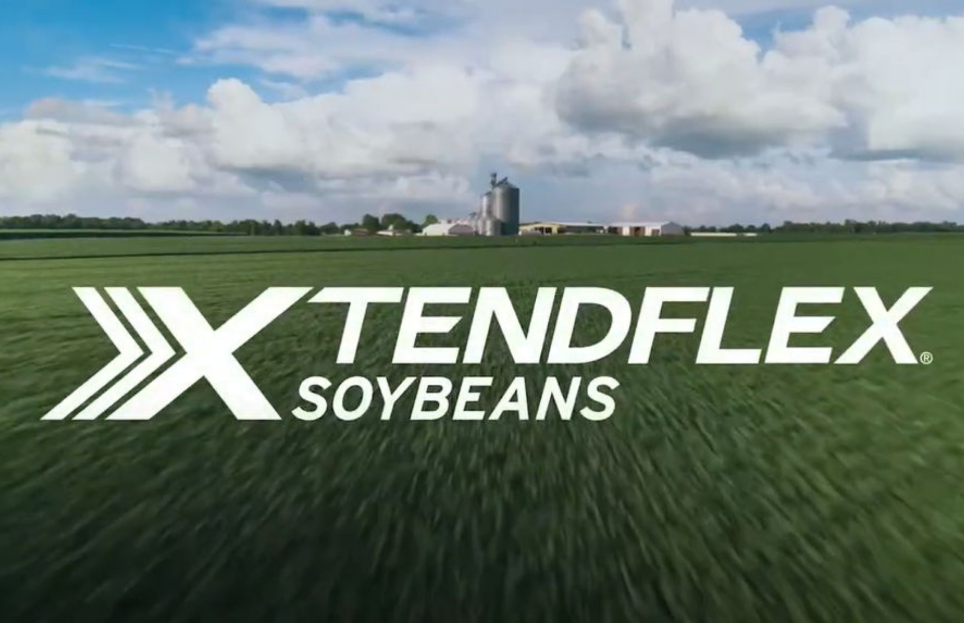 XtendFlex soybeans logo over a green soybean field with farm buildings and cloudy sky in the background.