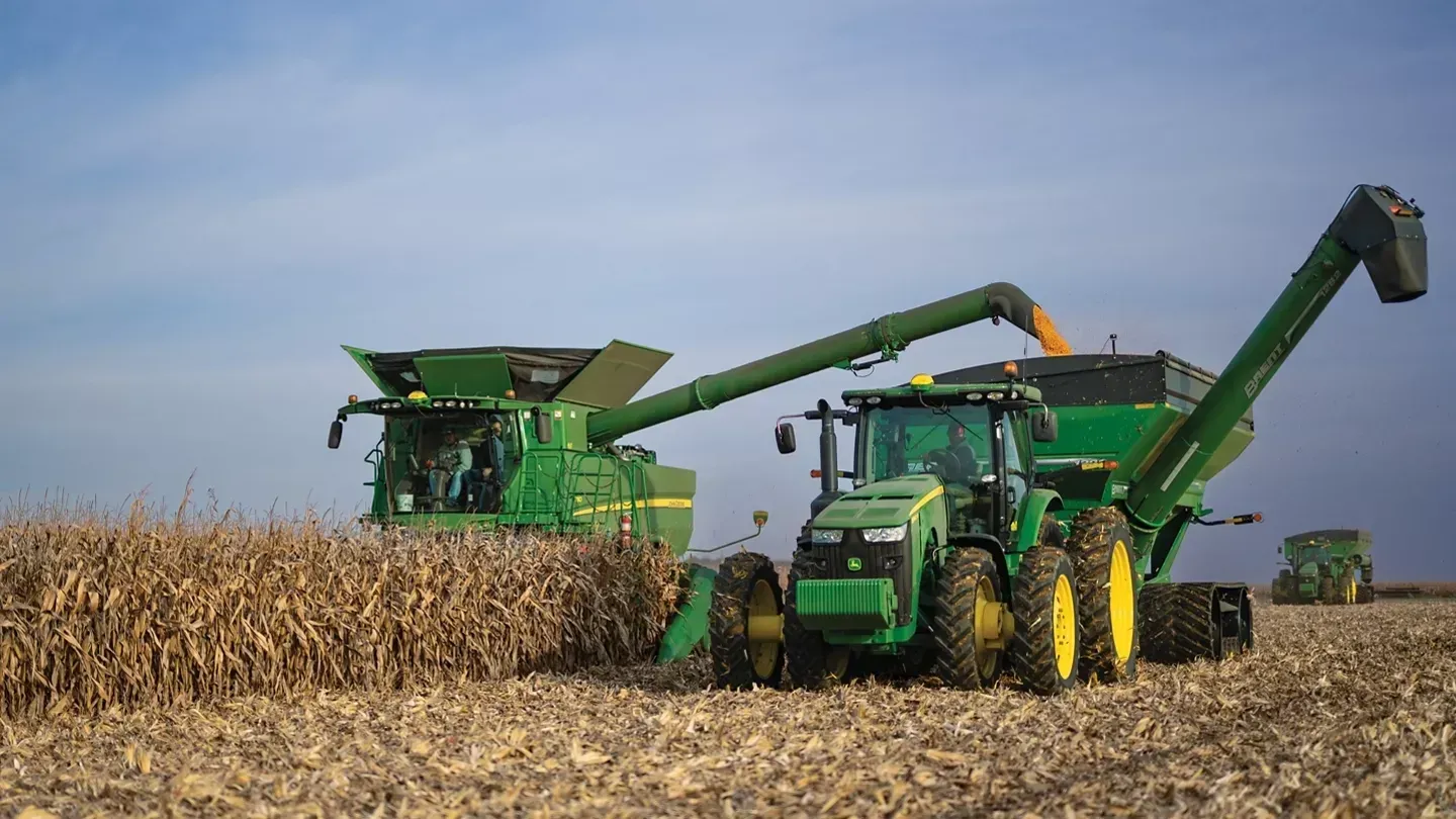 Green farm equipment harvesting corn in a field under a blue sky.
