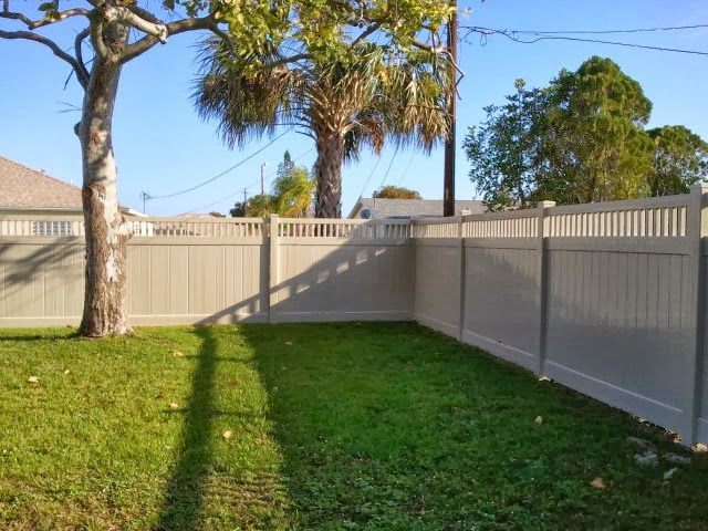 A white fence surrounds a lush green yard with trees in the background.
