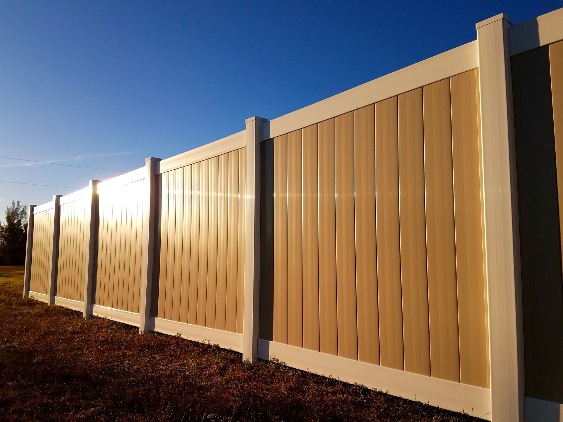 A tan and white fence with a blue sky in the background