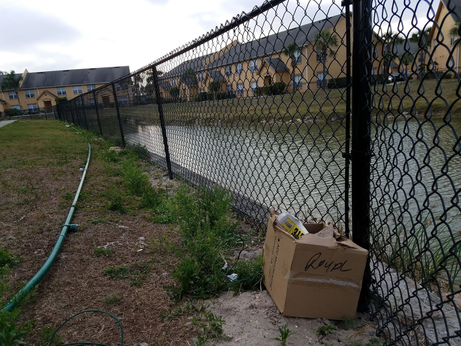 A cardboard box with the word grocery written on it is sitting next to a chain link fence.
