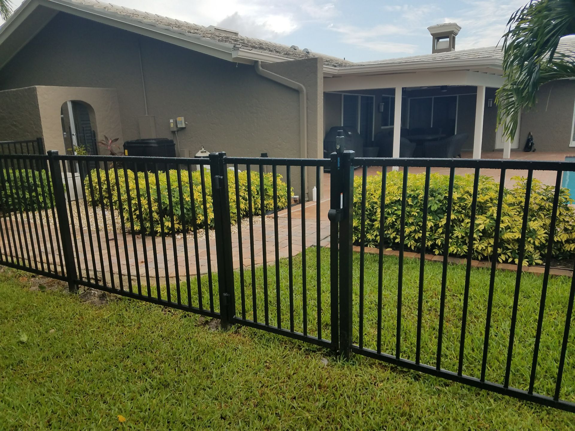 A black fence surrounds a lush green yard in front of a house.