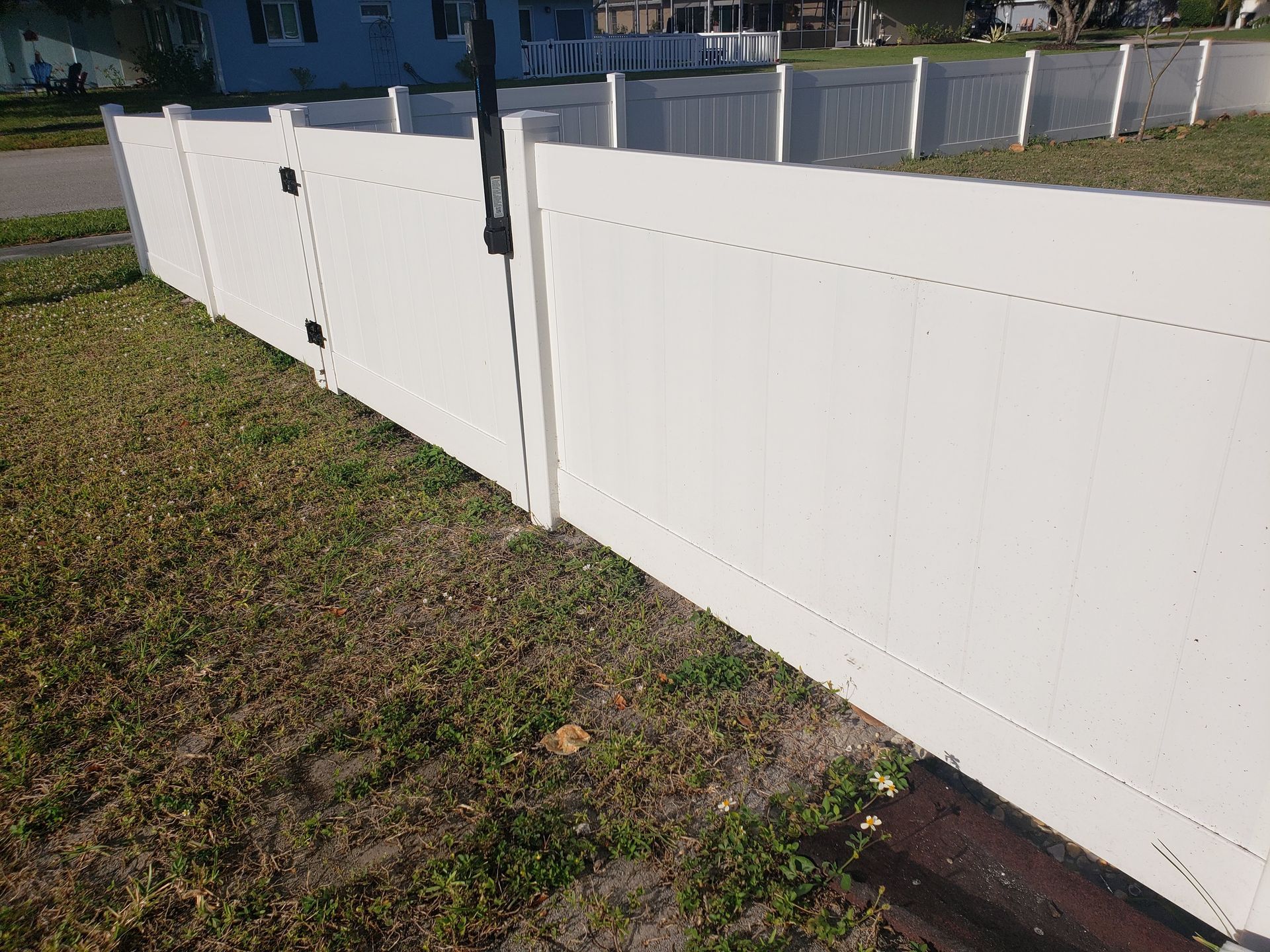 A white fence is sitting in the grass next to a house.