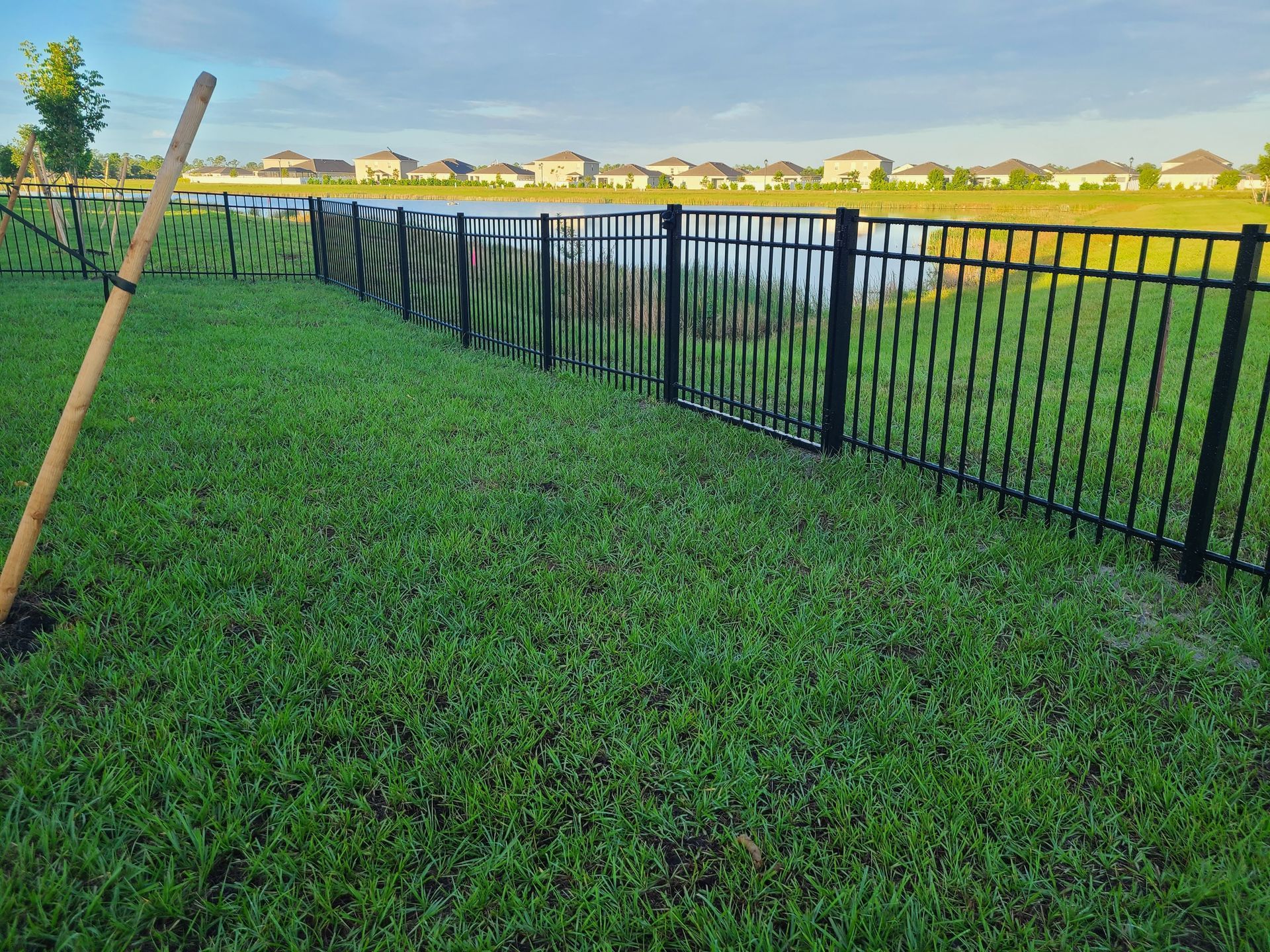 A black fence surrounds a lush green field with a shovel in the grass.