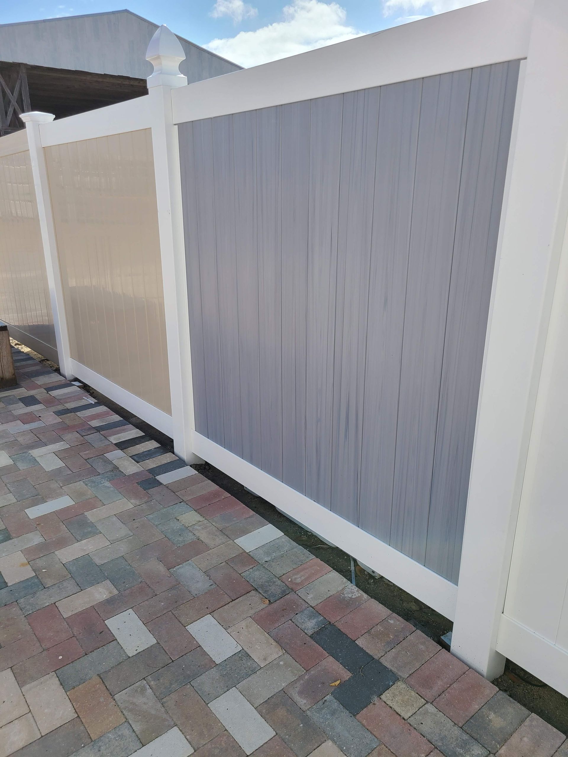 A white fence is sitting on top of a brick driveway.