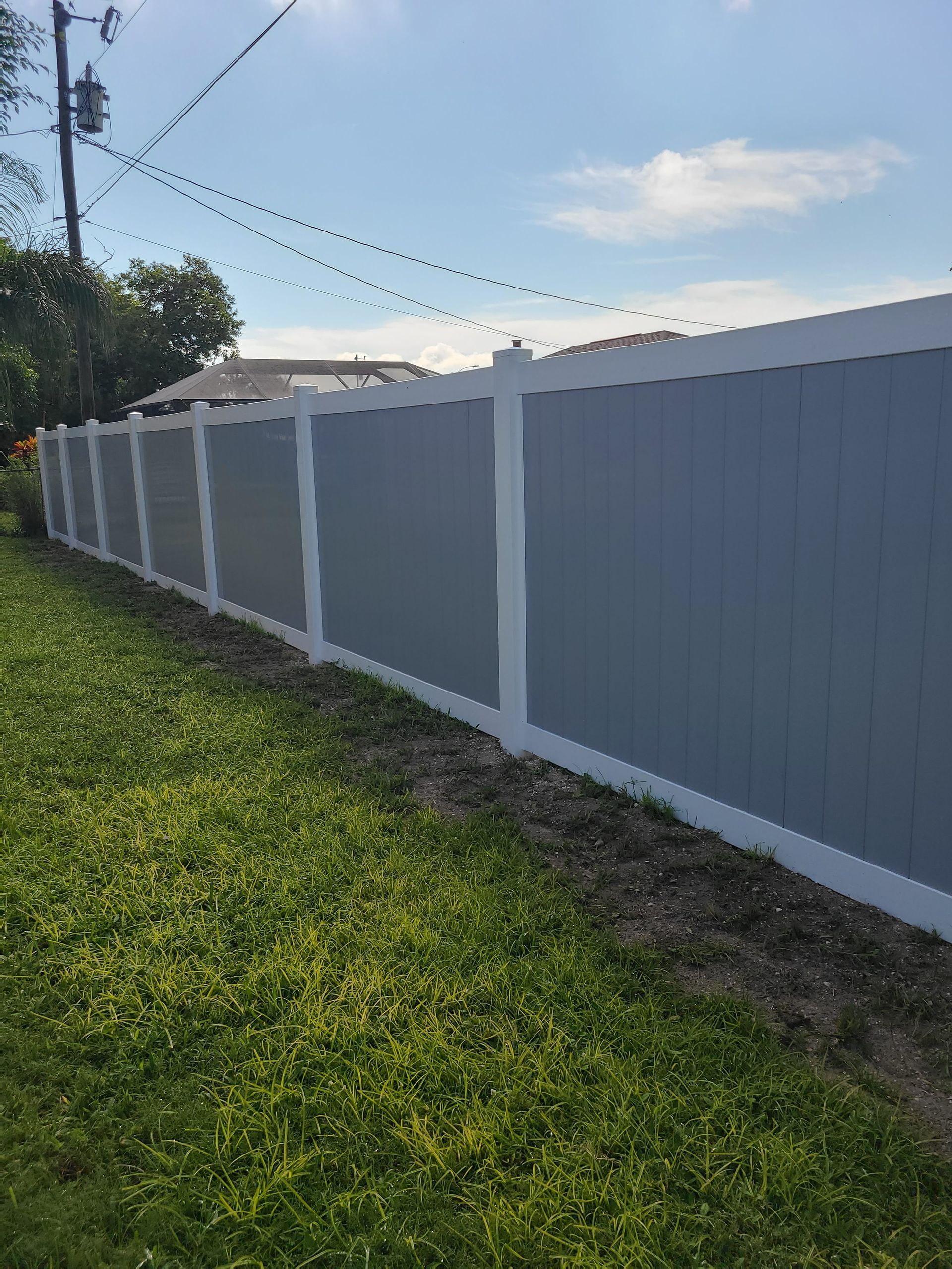 Gray and white vinyl privacy fence along a green lawn under a sunny sky.