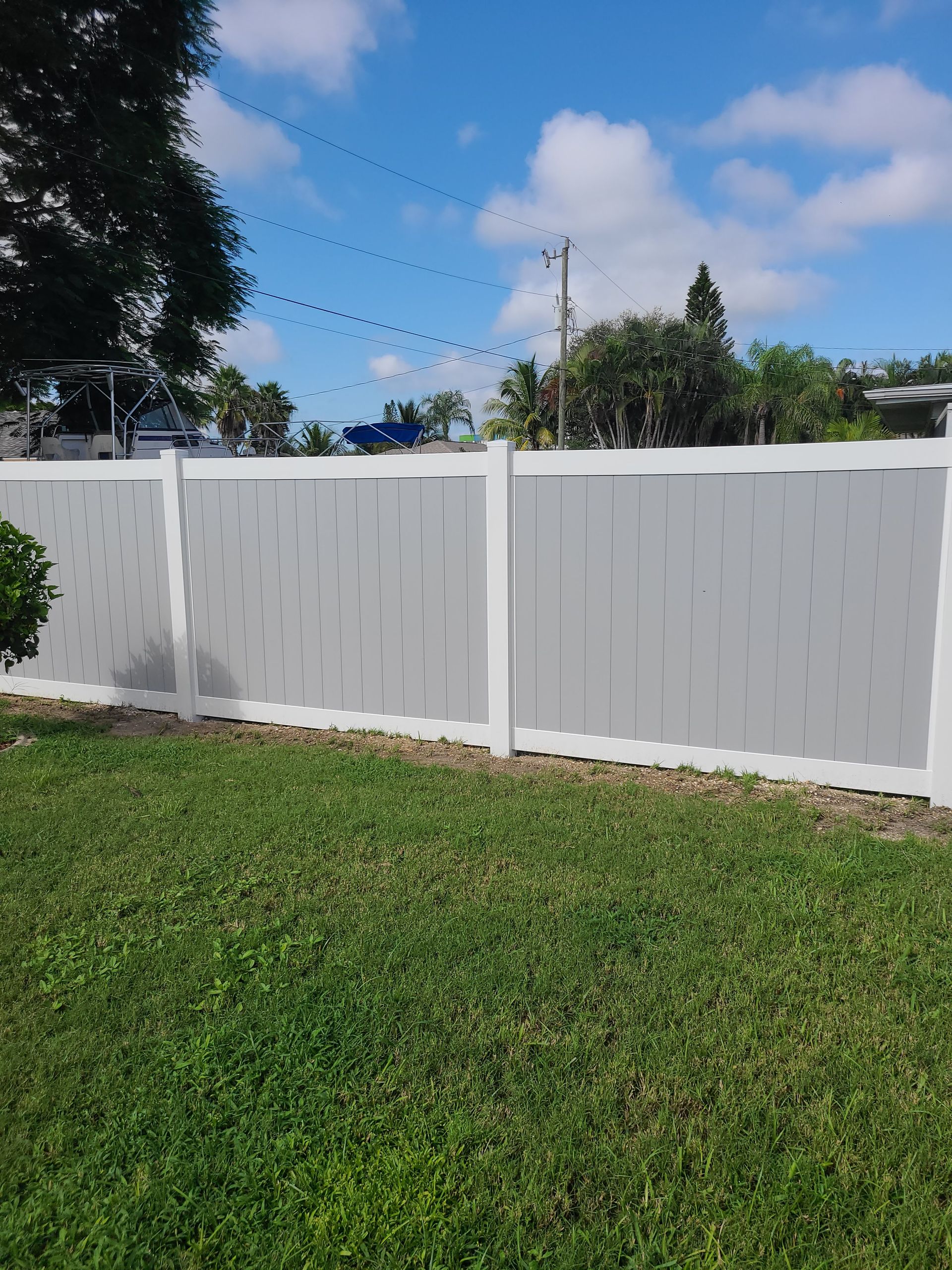 Gray and white vinyl fence in a grassy yard, with blue sky in background.