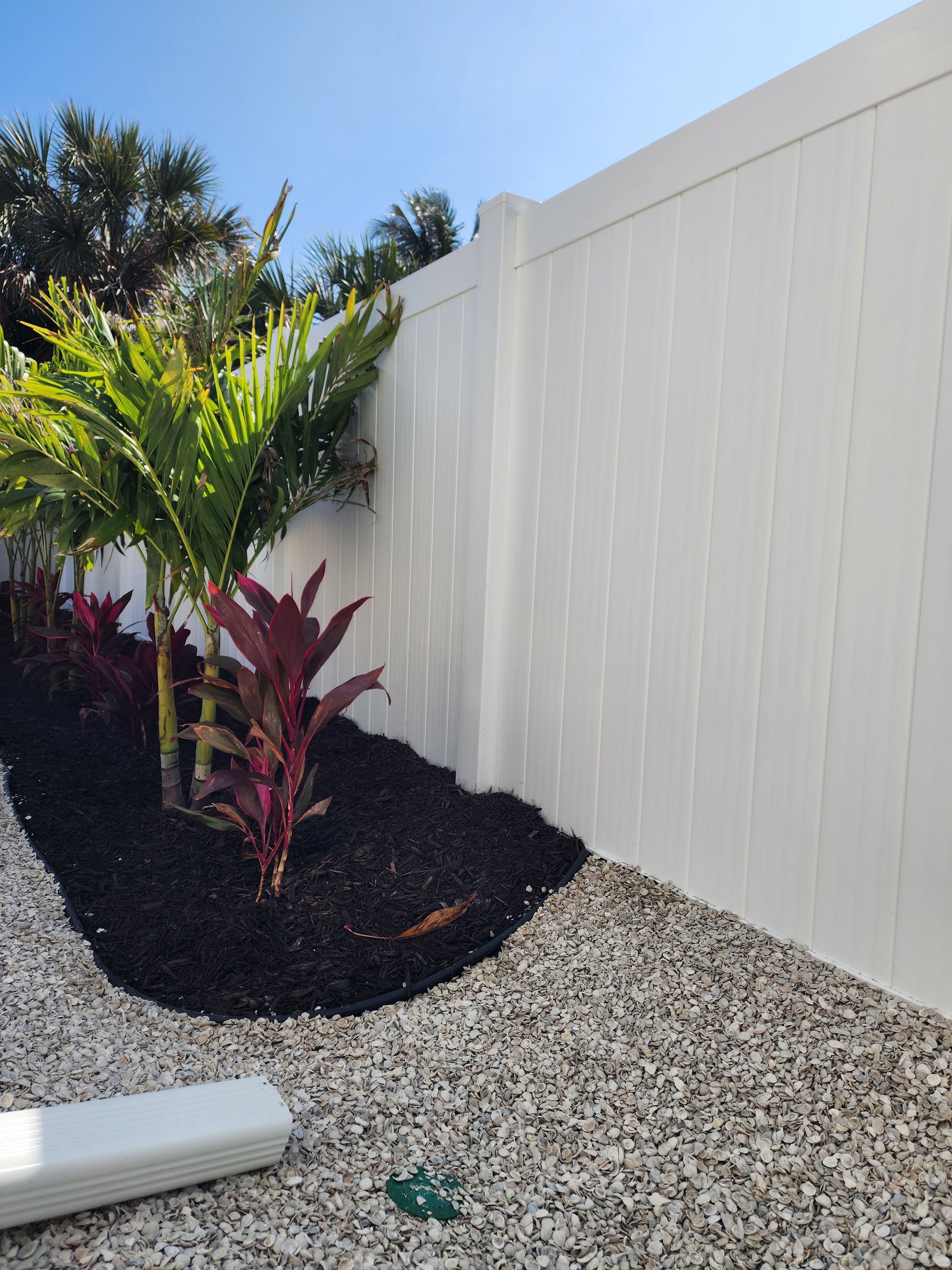 A white fence surrounds a garden with plants and gravel.