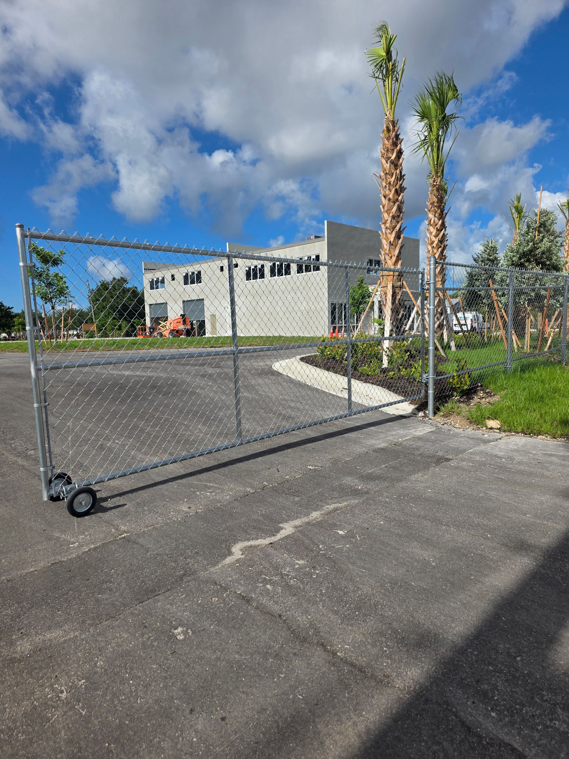 Open chain-link gate on a paved lot in front of a modern white building under a blue sky