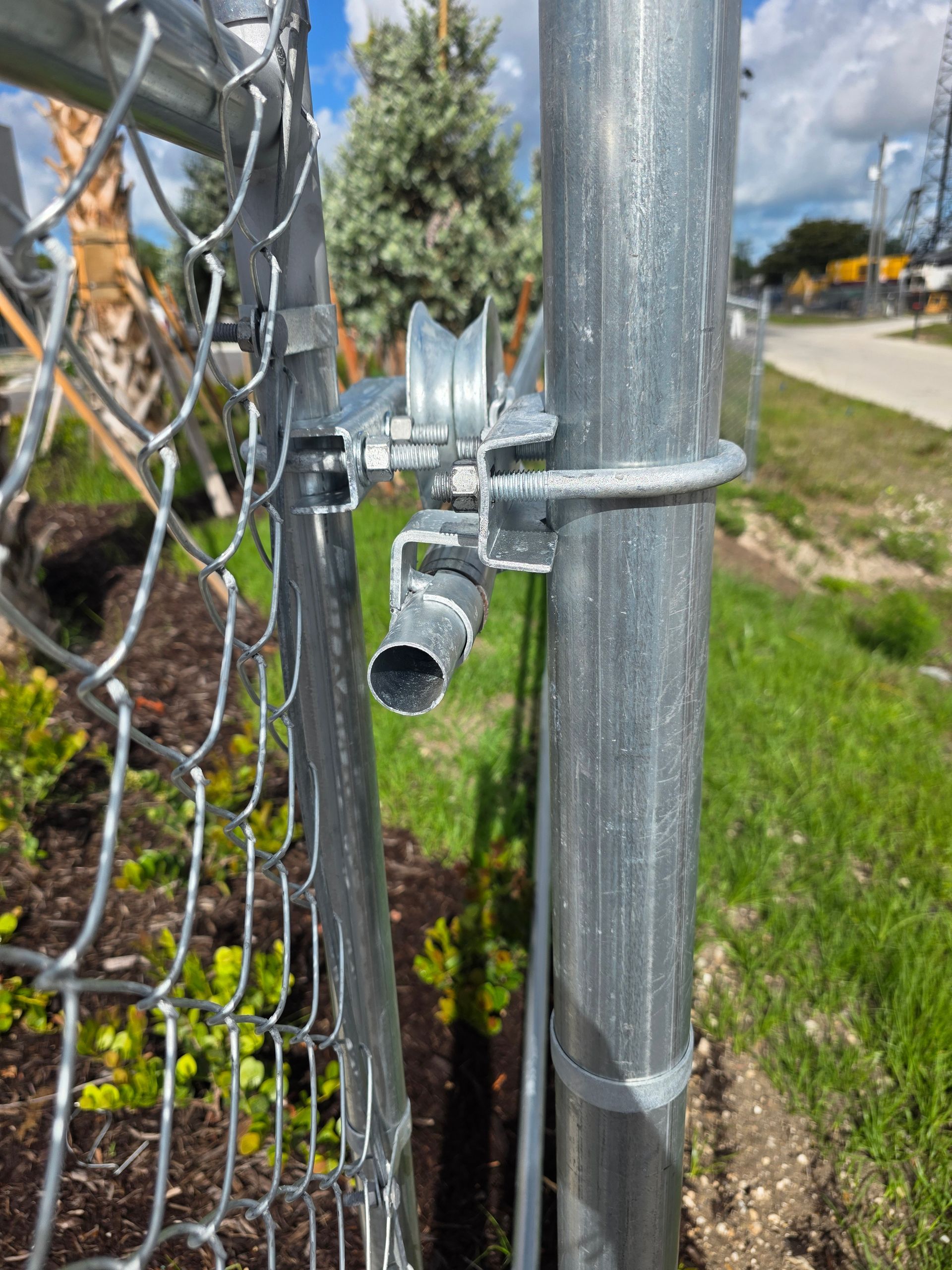 Chain-link gate latch on a galvanized metal fence beside a grassy roadside.