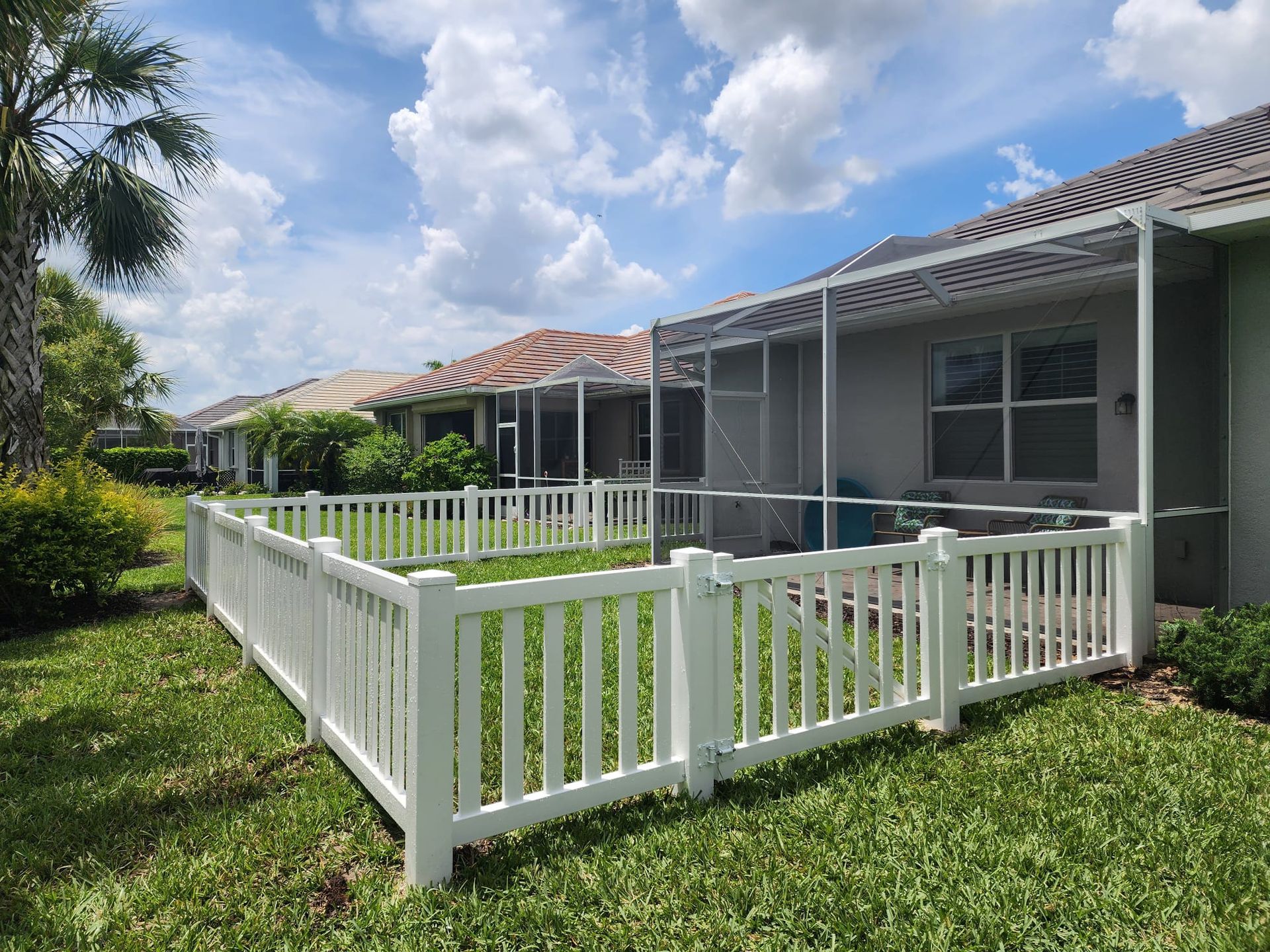 A white fence surrounds a screened in porch in front of a house.
