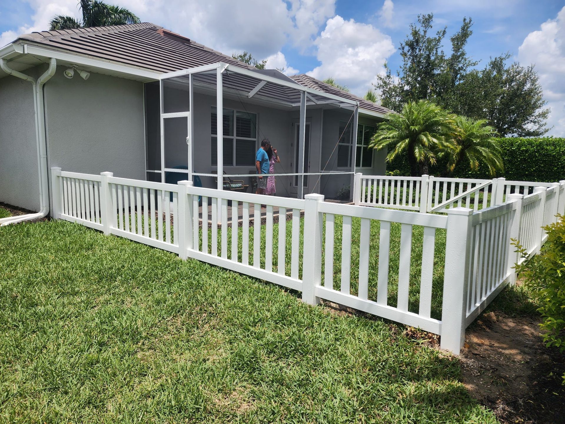 A white fence surrounds a screened in porch in front of a house.