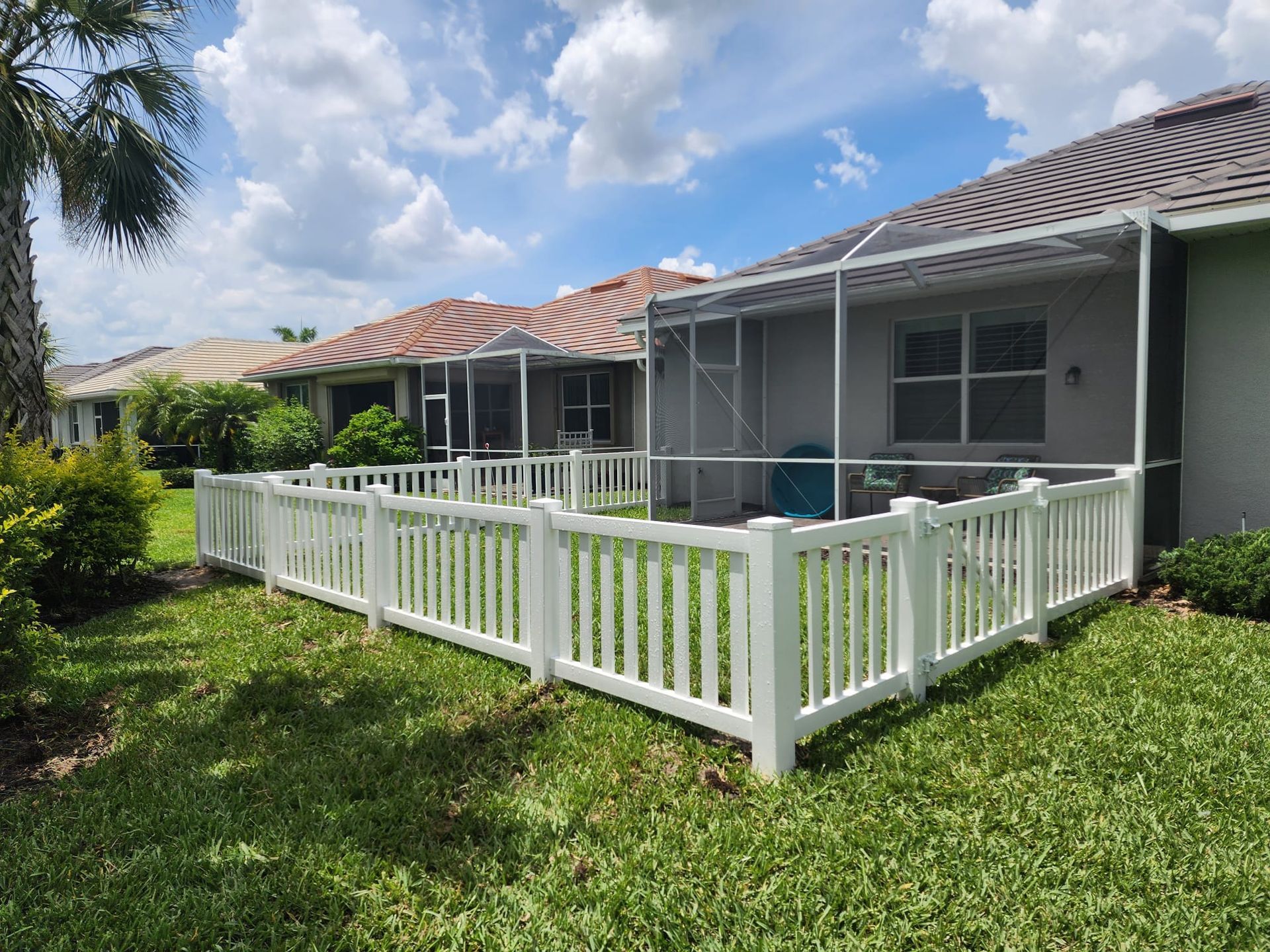 A white fence surrounds a screened in porch in front of a house.