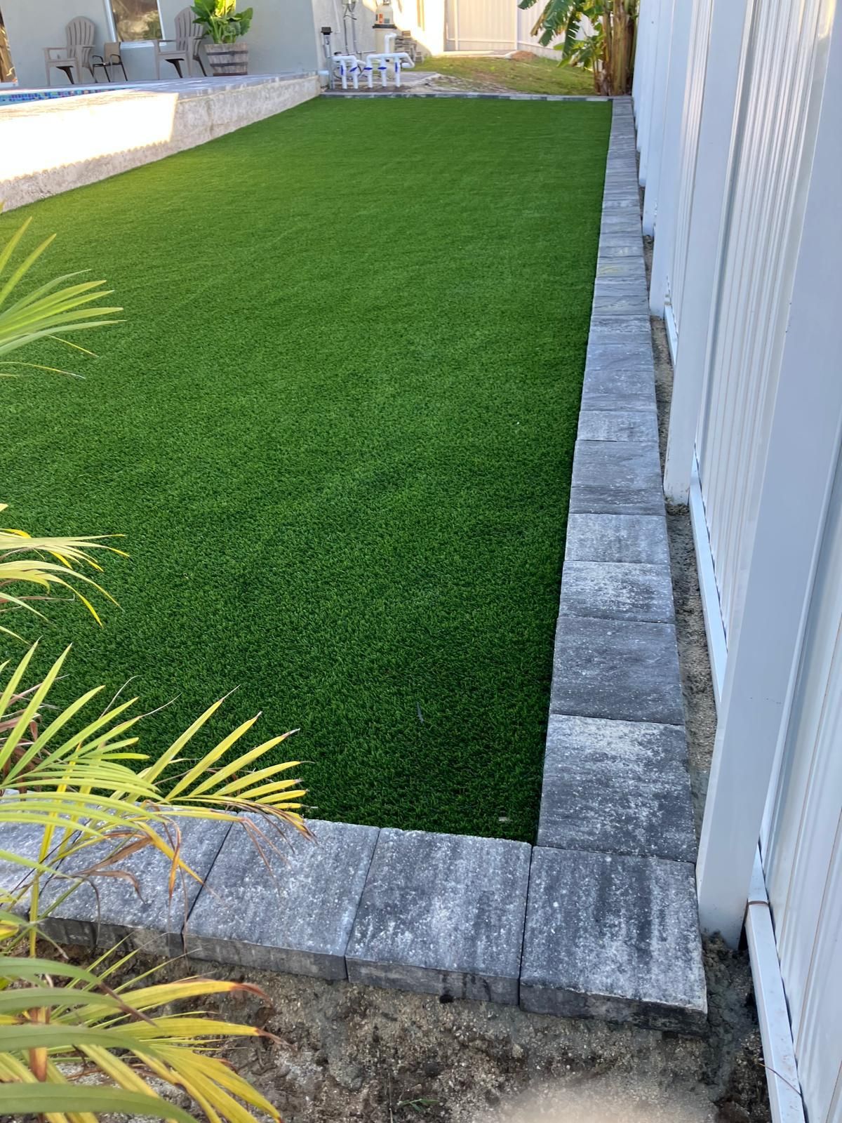 Green artificial turf lawn bordered by gray stone blocks and white fence.