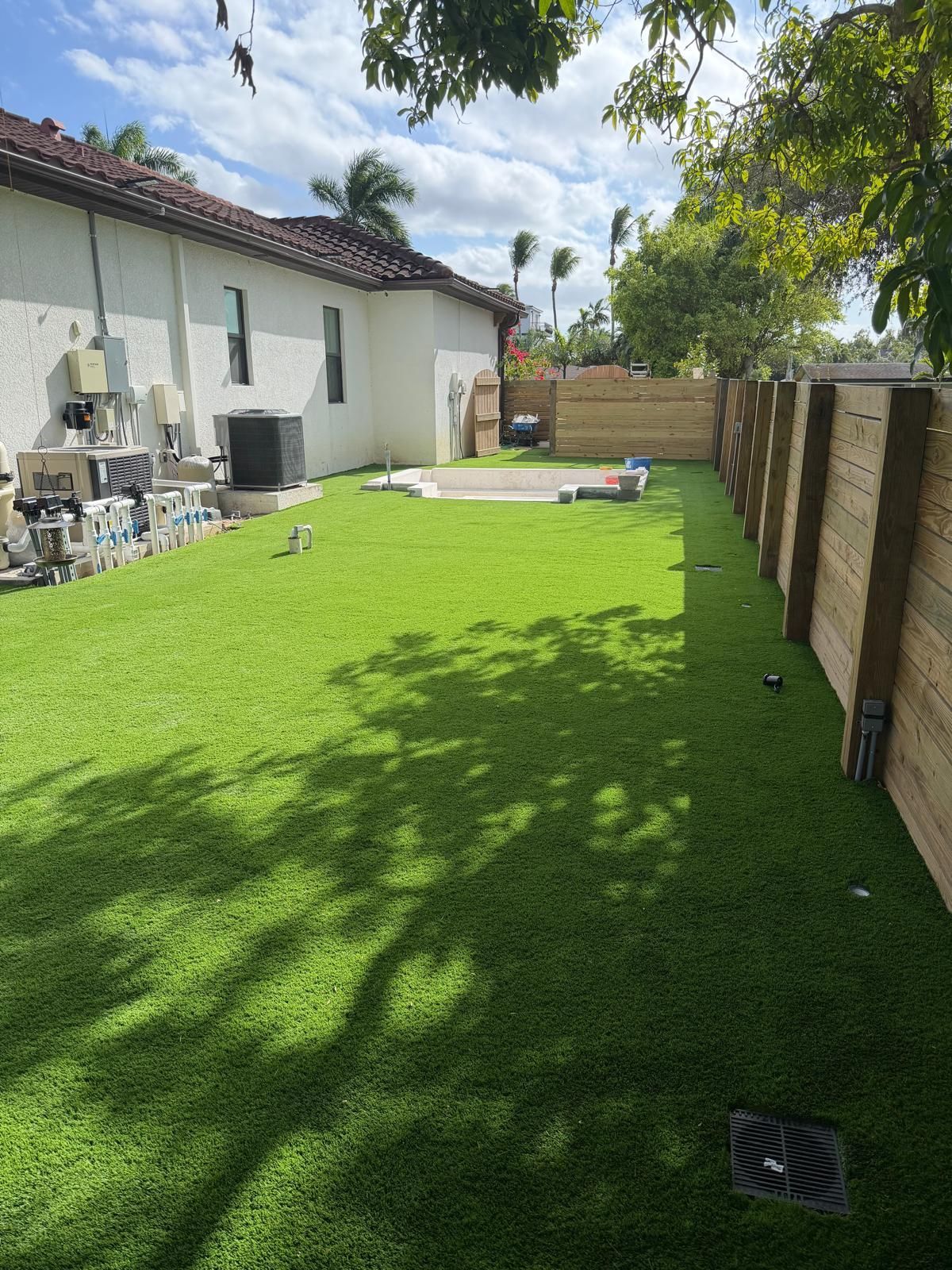 Backyard with green turf, wooden fence, white house, and overcast sky.