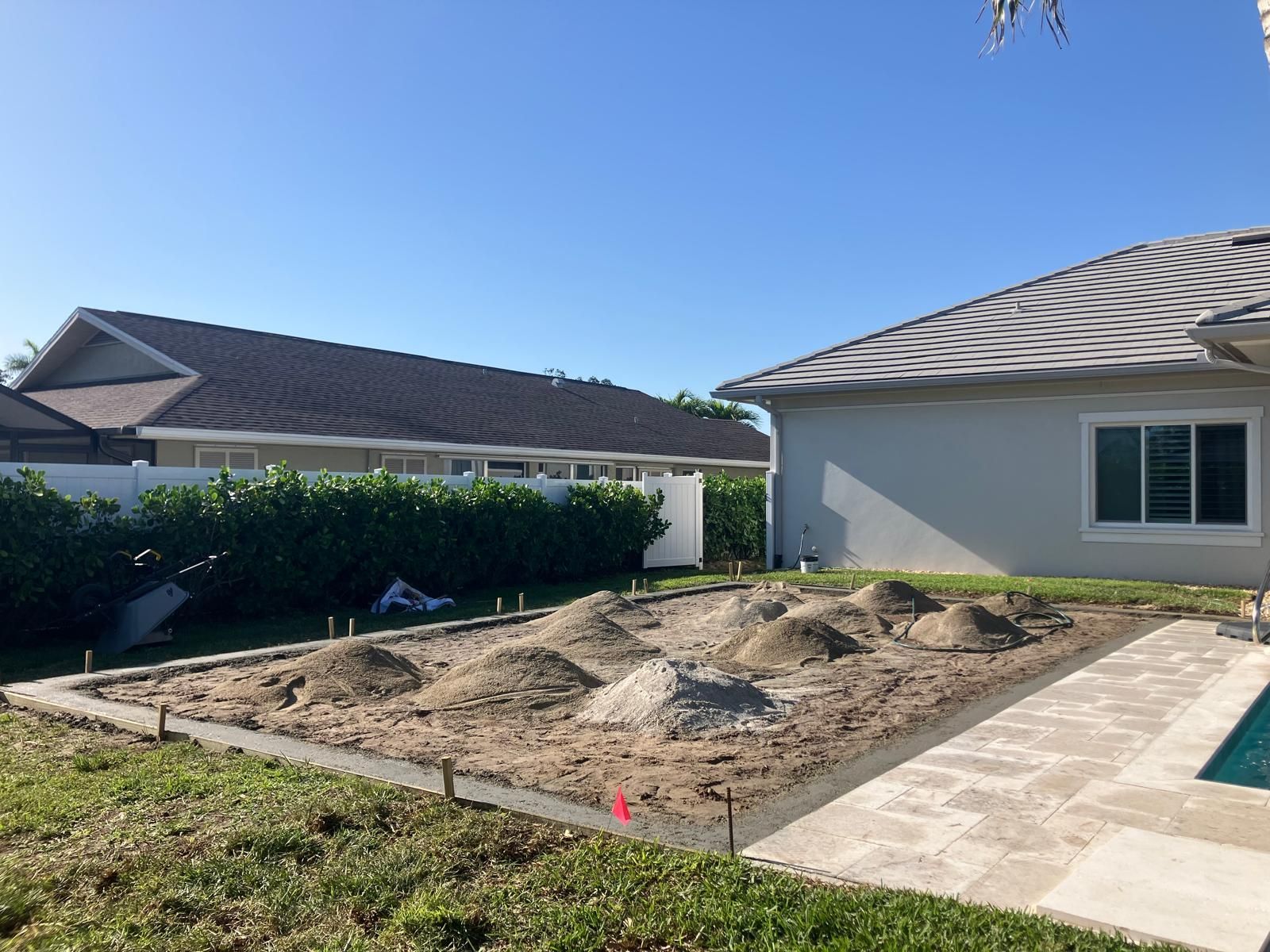 Backyard with a concrete frame, piles of dirt, and a house.