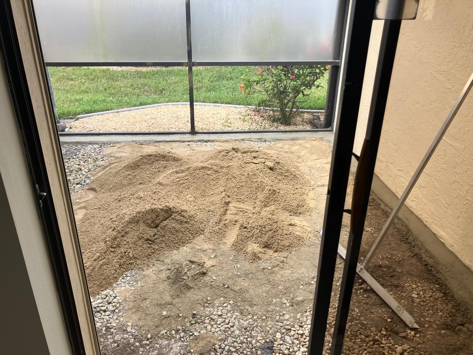 Doorway view of a patio with dirt pile, gravel, grass, and a partially obscured plant, enclosed by a black metal frame.