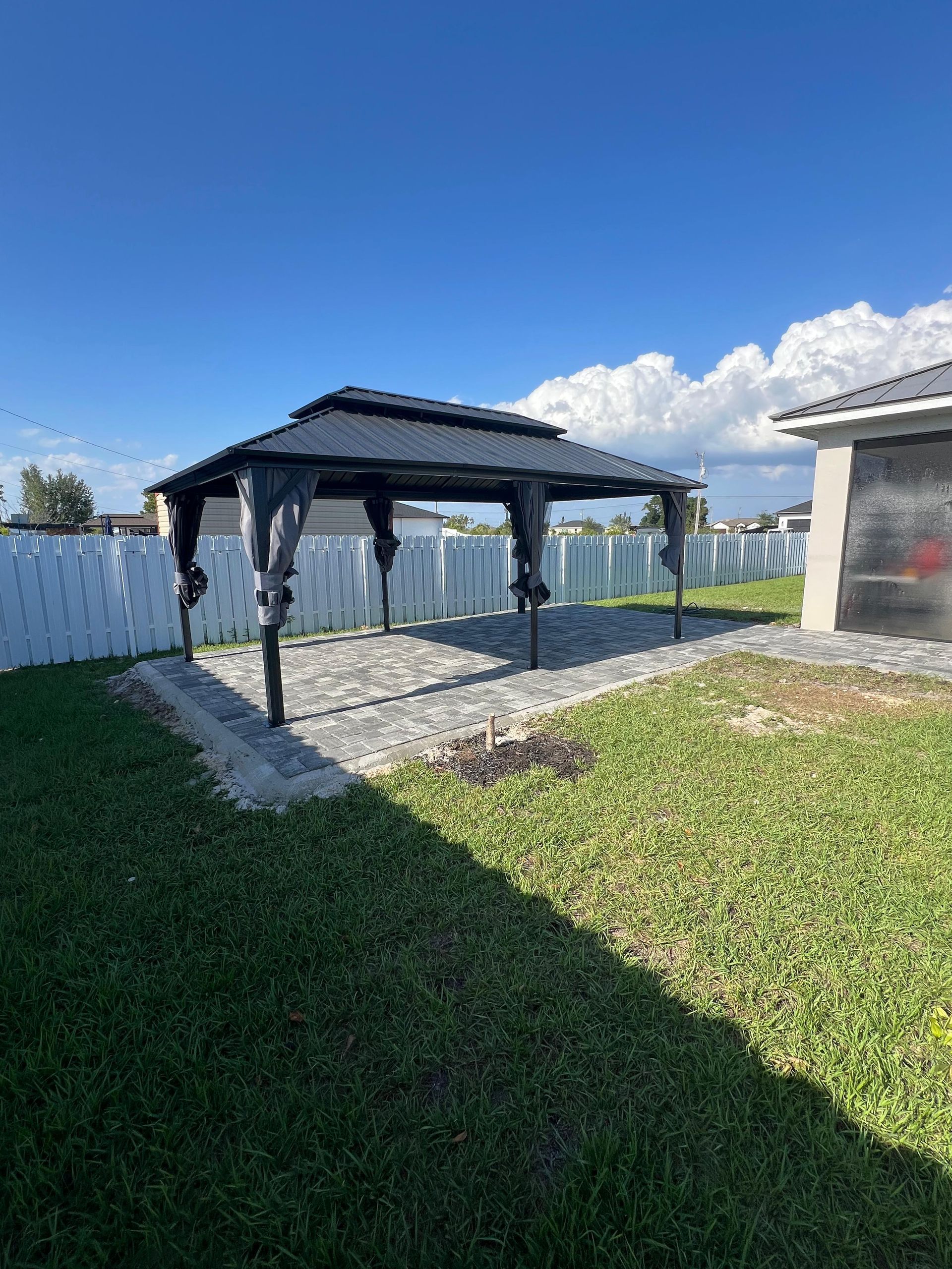 Gazebo on a brick patio in a backyard with a blue sky.