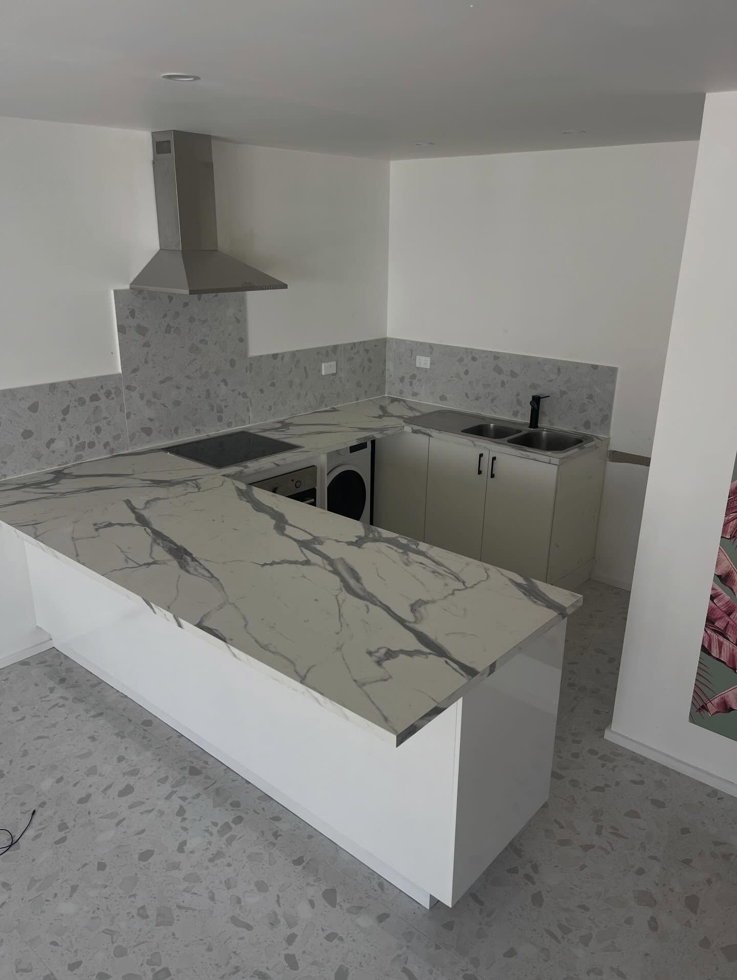 A modern kitchen with white cabinets, a marbled countertop island, a stainless steel range hood, and gray tiled flooring.