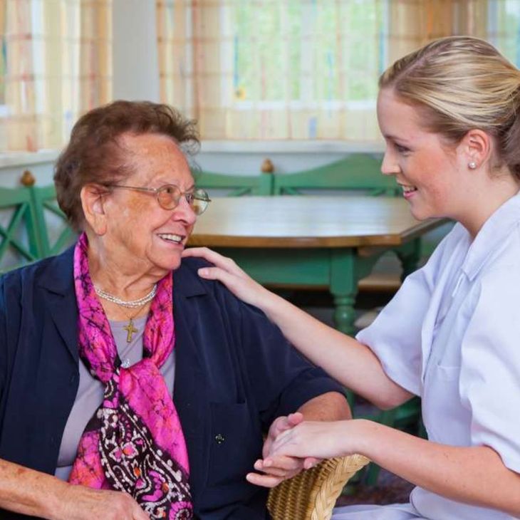 A nurse is putting her hand on an older woman 's shoulder